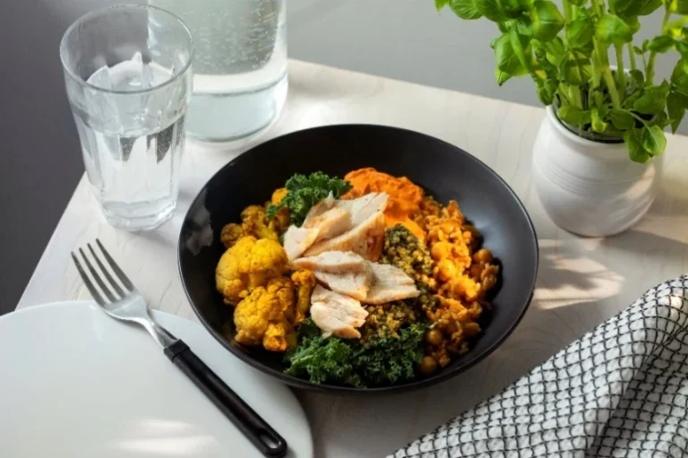 Hetki Bistro -mikroateria annosteltuna mustaan kulhoon: kanaa, paahdettua kukkakaalia, lehtikaalia ja romesco-kastiketta